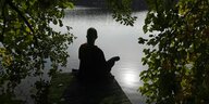 Frau sitzt allein auf einem Steg an einem See und meditiert