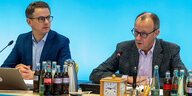 Carsten Linnemann und Friedrich Merz sitzen an einem Tisch - vor sich ganz viele Wasser- und Colaflaschen, im Hintergrund eine himmelblaue Wand