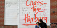 Auf einer Wand steht ein Graffiti "Chaostage Hamburg", davor sitzt eine Frau mit Kind