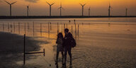 Mann und Frau im Sonnenuntergang am Strand vor Windkraftanlagen