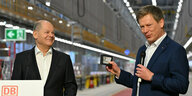 Olaf Scholz schaut lächelnd zu Bahnchef Richard Lutz, er ihm eine Geschenkkarte zeigt