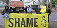 Fünf Menschen protestieren mit Porträts der Hingerichteten im Iran und einem großen Transparent auf dem "Shame" steht