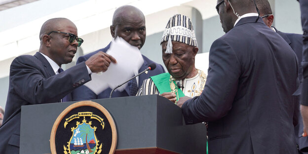 Leibwächter von Präsident Joseph Boakai fächeln ihm mit einem Papier frische Luft zu, er wirkt geschwächt