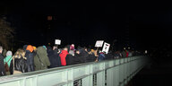Menschen gehen in der Dunkelheit mit Protestplakaten gegen die AfD über eine Brücke
