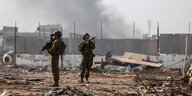 Zwie israelische Soldaten schauen ratlos in die Luft. Hinter ihnen stegt Rauch auf, sie stehen in einm Trümmerfeld