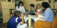 Fünf Jugendliche sitzen in einem Zimmer im 80er Jahre Ambiente mit Schrankwand und Flokati Teppisch auf dem Boden oder Sofa und rauchen und trinken
