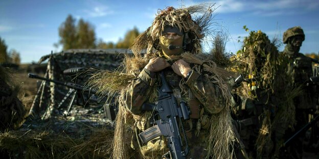 Bewaffnete Bundeswehrsoldaten im Feld in Tarnuniform, sie sehen aus wie ein zerfledderter Busch