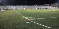 eine Gruppe Frauen trainiert auf einem Fußballplatz, vor ihnen liegt eine umgeworfene Eckfahne mit Palästina-Fähnchen