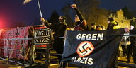 Linke Aktivisten in Chemnitz heben eine Fahne und die Faust hinter einem Transparent mit einem durchgestrichenen Hakenkreuz und der Aufschrift "Gegen Nazis".
