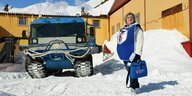 Ein weibliches Mitglied der Wahlkomission steht mit einer tragbaren Wahlurne neben einem blauen Schneeräumer auf einem schneebedeckten Platz