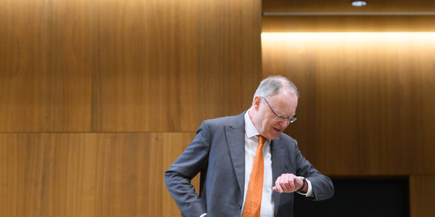 Ministerpräsident Stephan Weil steht im Landtag und blickt auf seine Armbanduhr