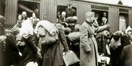 Deutscher Juden und Jüdinnen stehen dicht gedrängt mit Koffern und Taschen vor einem Deportationszug