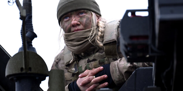 Soldatin mit blondem Zopf unter einer Mütze und GEsichtsbemalung