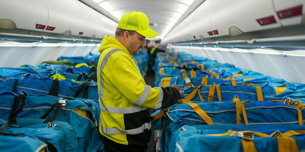 Ein Angestellter der Post steht im Frachtraum eines Flugzeugs umgeben von blauen Postsäcken