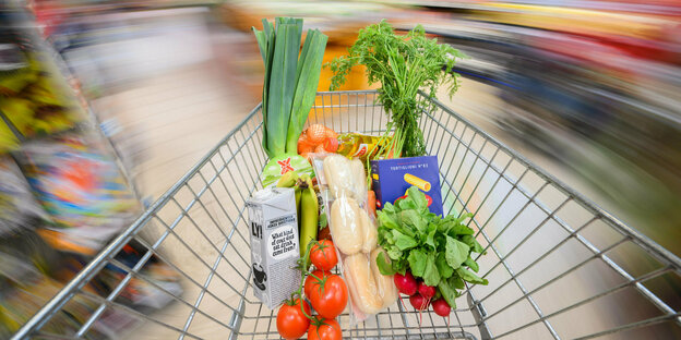 Ein mit Lebensmittel gefüllter Einkaufswagen wird durch einen Supermarkt geschoben