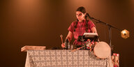 Die Musikerin hält rechts einen Trommelschlegel, vor ihr auf dem Tisch diverse elektronische Instrumente