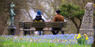 Sibirischer Blaustern (Scilla siberica) und Narzissen blühen, während Passanten auf einer Parkbank sitzen