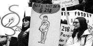 Frauen stehen mit Plakaten, die für die Abschaffung des 3 218 werben auf einer Demonstration