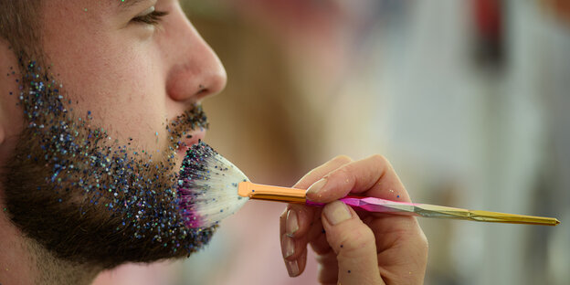 Ein Besucher lässt sich während des Lollapalooza Festivals im Olympiapark von einer Schaustellerin den Bart mit Glitzer verzieren.