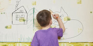 Ein Junge malt eine tapezierte Wand mit Buntstiften an