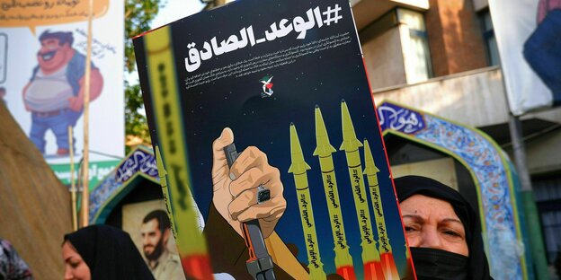 Eine in schwarzen Tschador gekleidete Iranerin hält bei einer Kundgebung ein anti-israelisches Plakat hoch, das Raketen zeigt