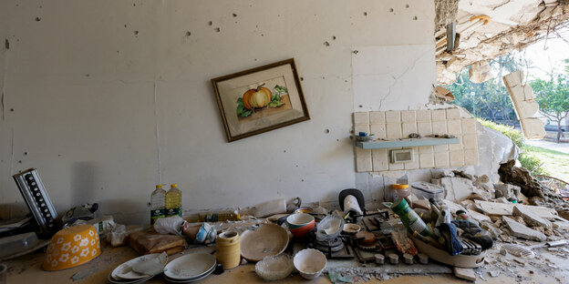 Eine Wand mit Einschusslöchern, Geschirr auf der Spülenablage, ein schief hängendes Bild