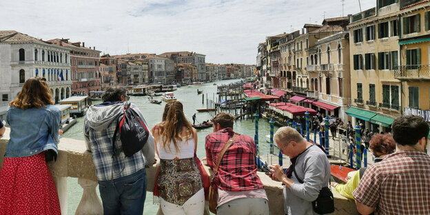 Touristen stehen auf der Rialtobrücke in Venedig und schauen auf den Canal Grande.
