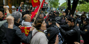 Eine Demonstrationsteilnehmerin streitet mit Polizisten, im Hintergrund recken menschen ihre Fäuste und schwingen rote Fahnen