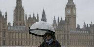 EIne Frau mit Schirm in London vor dem Houses of Parliament