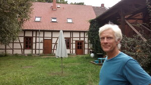Ein Mann in blauem Pullover steht vor einem Hof. Ein Mann in blauem Pullover steht vor einem Hof.