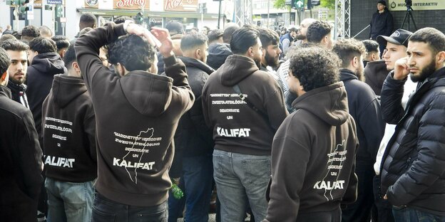 Junge bärtige Männer tragen Hoodies, auf dem Rücken die Forderung nach einem Kalifat.