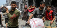 Menschen tragen in einer zerstörten Stadtlandschaft Säcke auf ihren Schultern