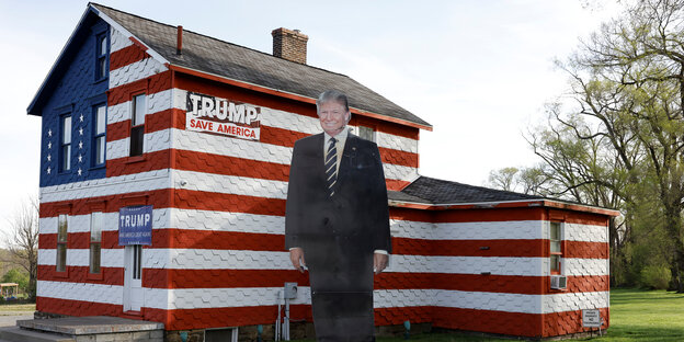 Ein Haus, das in den Farben der US-amerikanischen Flagge gestrichen ist, im Vordergrund eine lächelnde Donald-Trump-Pappfigur
