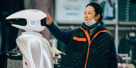Eine Frau steht einem humanoiden Roboter gegenüber und streichelt seinen Kopf
