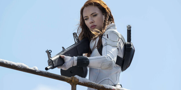 Scarlett Johansson holds a gun and looks down from a scaffold.