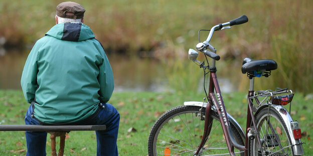 An older man sitting on a park bench with a bicycle next to him