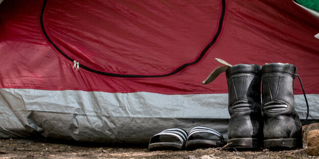 Schmutzige Stiefel und Badelatschen vor einem Zelt