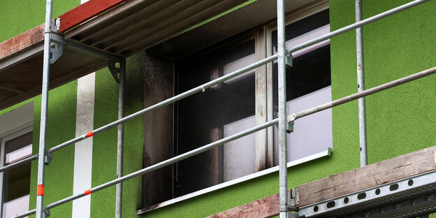 Ein Baugerüst steht vor dem Fenster. Der Rahmen ist verkohlt vom Brandanschlag