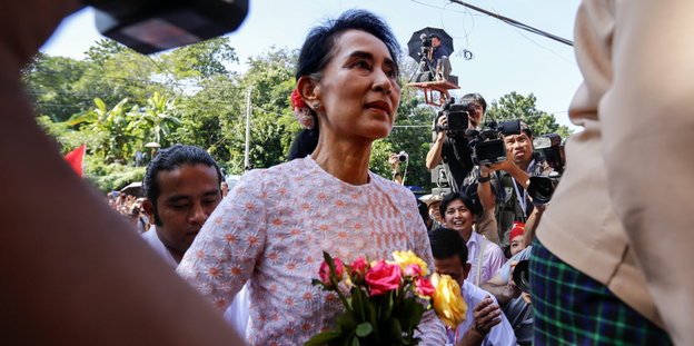 Eine Frau mit Blumen in einer Menschenmenge - es ist die Wahlsiegerin Aung San Suu Kyi