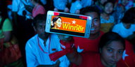 Ein blau angeleuchteter Mensch hebt ein Smartphone mit der Display „We are the winner“ hoch