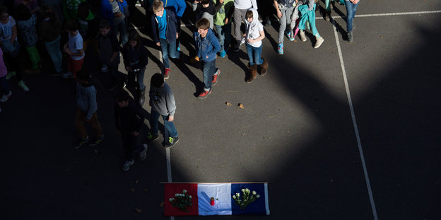 Schüler laufen an einer französischen Flagge vorbei, die auf dem Boden arrangiert ist