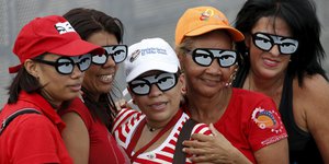 Unterstützerinnen von Präsident Nicolas Maduro posiereen mit Sonnebrillen, die die Augen von Hugo Chavez nachbilden.