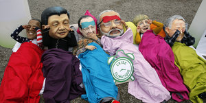 Aktivist*innen tragen Masken mit den Gesichtern von wichtigen Staatschefs und stellen sich schlafend