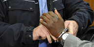 Polizist legt an das Handgelenk eines Mannes Handschellen an.