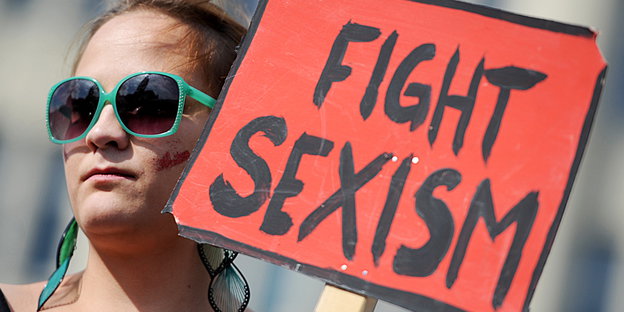 Frau mit Sonnenbrille hält ein Schild hoch, auf dem steht „Fight Sexism" Frau mit Sonnenbrille hält ein Schild hoch, auf dem steht „Fight Sexism"