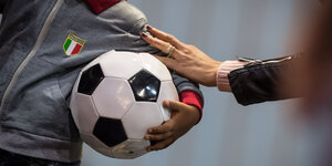 Ein Mensch hält einen großen Fußball im Arm, eine Frau hat ihre Hand auf seinen Arm gelegt