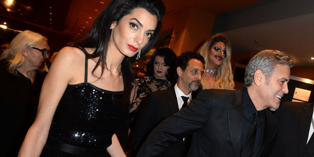 Links im Bild ist Amal Clooney, rechts ihre Ehemann. Im Hintergrund sind weitere Personen zu sehen