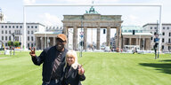 Das Foto zeigt Innensenatorin Iris Spranger (SPD) Arm in Arm mit Kultursenator Joe Chialo (CDU) auf Kunstrasen vor dem Brandenburger Tor.