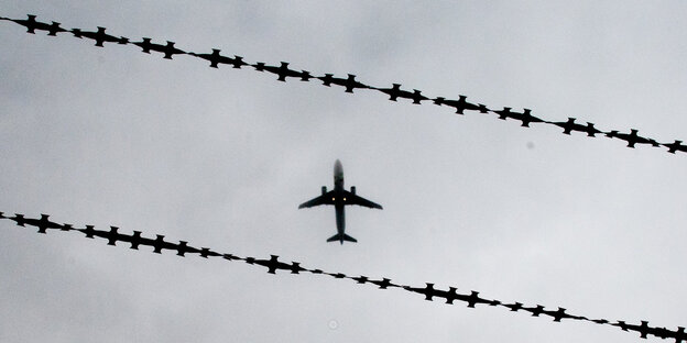 Ein Flugzeug ist am Himmel hinter Stacheldraht zu sehen.
