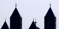 Kirchtürme einer Benediktinerabtei mit Kreuz auf dem Dach ragen schwarz vor hellem Himmel auf